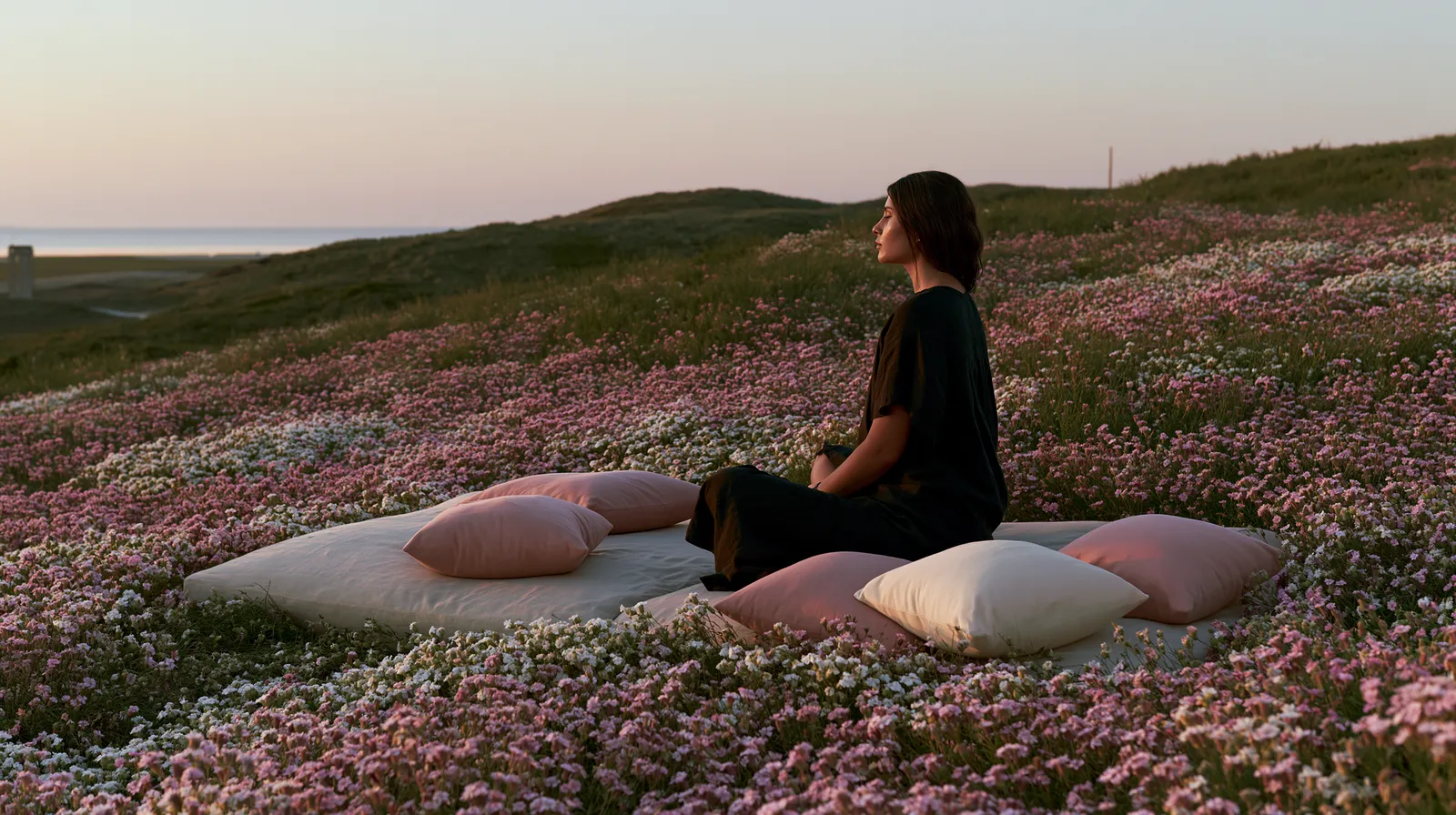 A woman meditating with eyes closed in a field of wildflowers at dusk